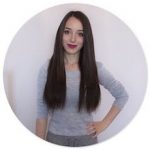 Mlada ženska z dolgimi ravnimi temnimi lasmi stoji na navadnem belem ozadju. Oblečena je v svetlo siv pulover z dolgimi rokavi in ima eno roko na boku. Nasmejana je in deluje samozavestno, pripravljena, da s svojim slogom po meri pusti pečat na domači strani SI.