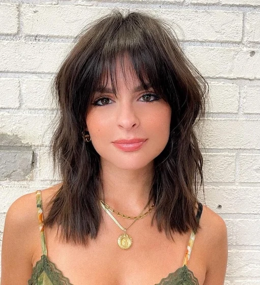 Ženska tankih las nosi teksturiran srednje dolg rez z frufrujem, frizura ustvarja videz več volumna in gibanja pri tankih laseh.