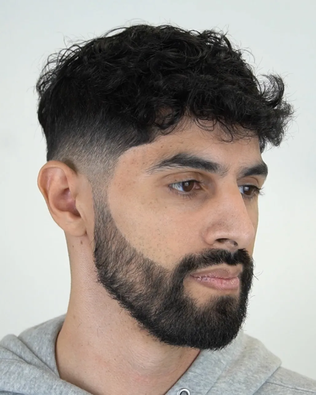 Kodrasta frizura z low fade prehodom in brado.