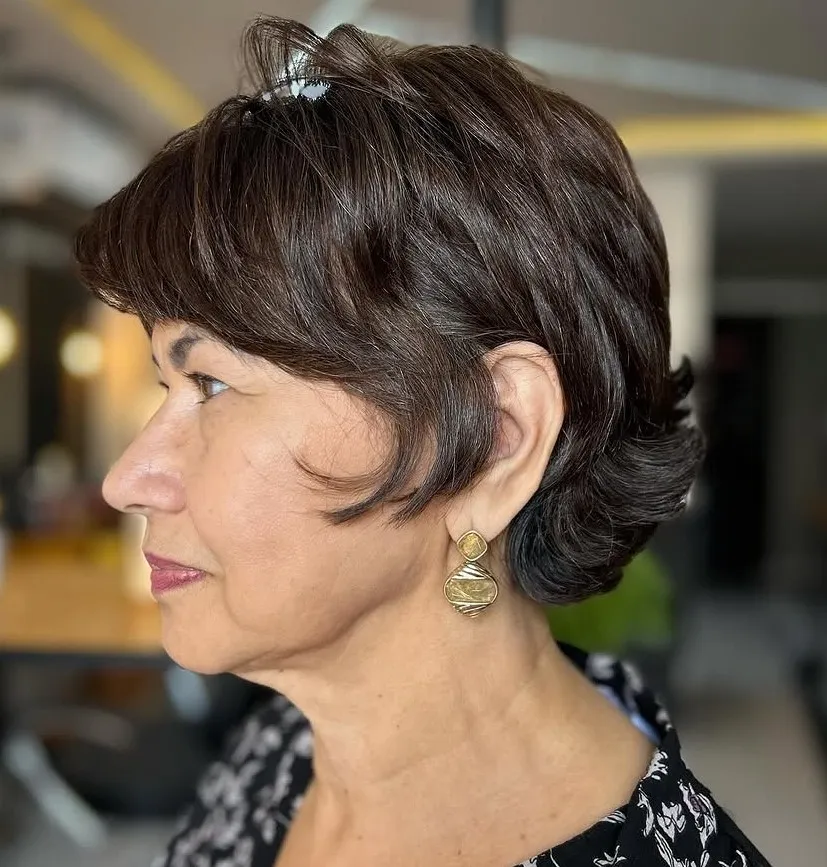 Razplasteni bixie paž z daljšimi prameni ob obrazu in lahkotnim volumnom po 60. letu.